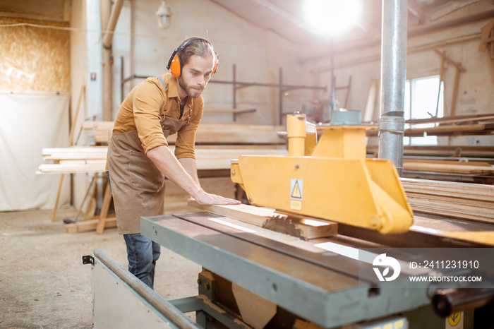 Carpentry worker sawing wooden planks with circular saw in the joinery warehouse