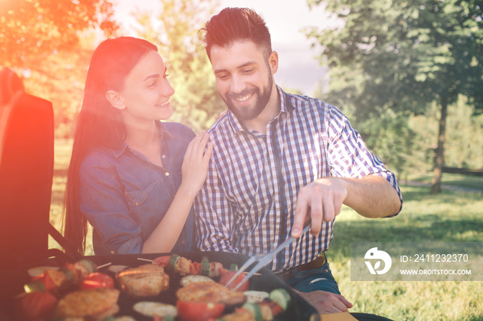 Friends making barbecue and having lunch in the nature. Couple having fun while eating and drinking 