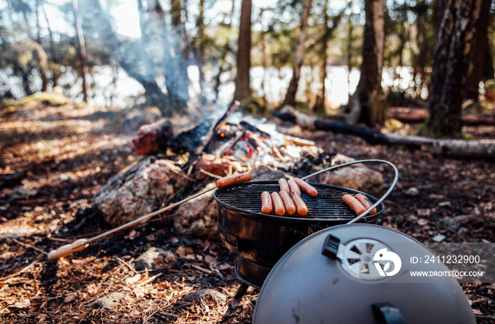 Grill hot dogs in the forest by a fire at a lake