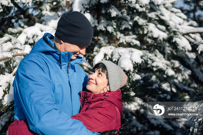 Middle age couple hug at the snowy winter park. A man and a woman in blue and red jackets having fun