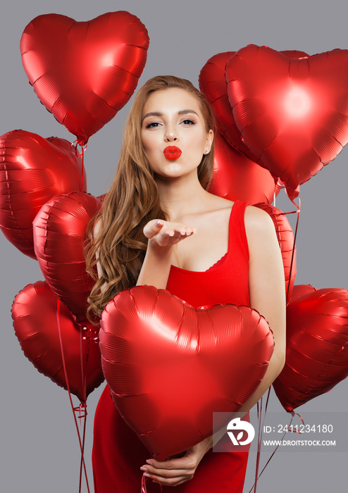 Young beautiful woman blowing kiss and holding red balloons. Model girl with red lips makeup wearing