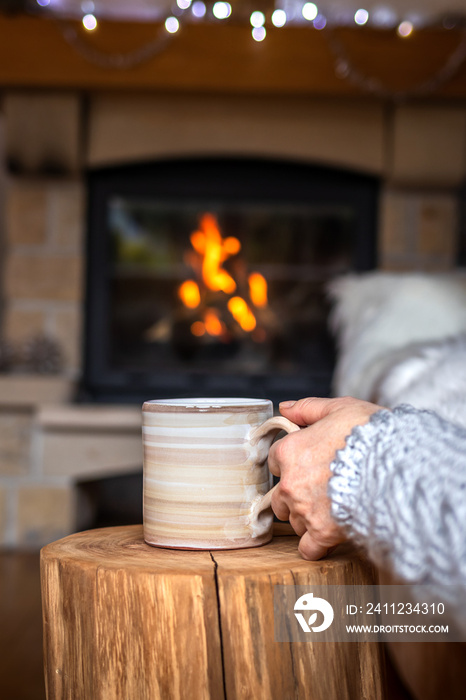 Relaxation with cup of coffee near fireplace. Woman resting with hot drink during christmas holiday