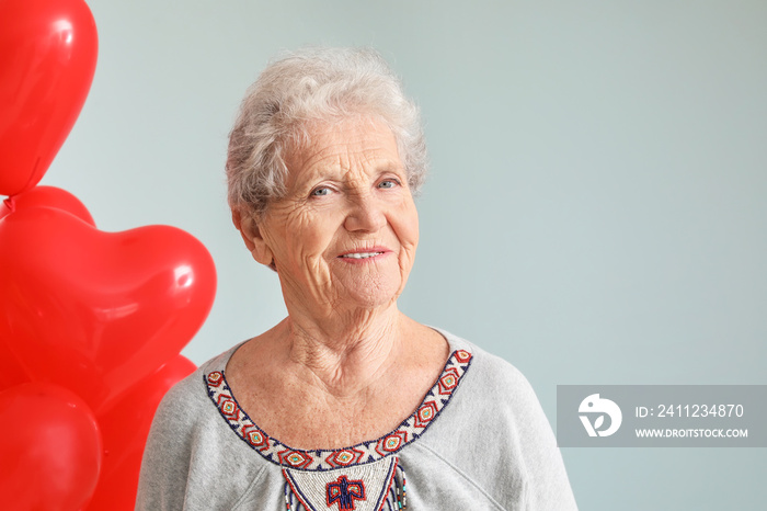 Portrait of senior woman with heart shaped air balloons on grey background