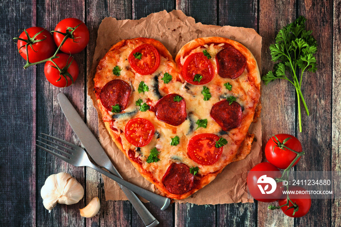 Heart shaped pizza for Valentines Day over a dark wood background. Top view, table scene with ingred