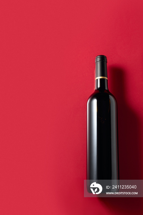 An unopened bottle of red wine on a red background.