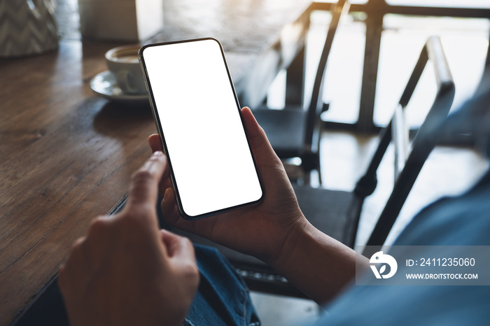 Mockup image of a woman holding and using mobile phone with blank white desktop screen with coffee c