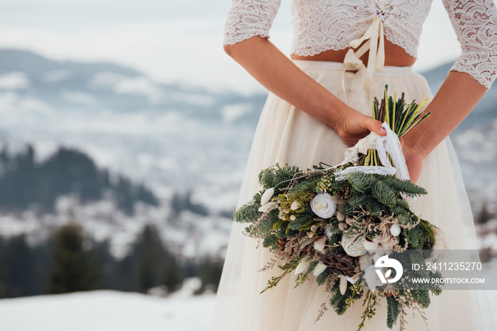 Beautiful bride in a white wedding dress holding her wedding bouquet in the mountains