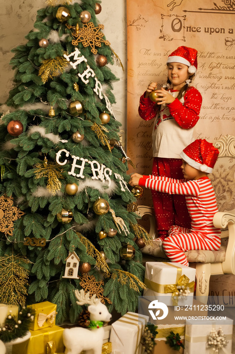 Happy children sit together on a chair near the Christmas tree