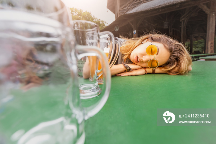 Young drunk Asian girl with hangover sleeping in Biergarten with empty beer mugs