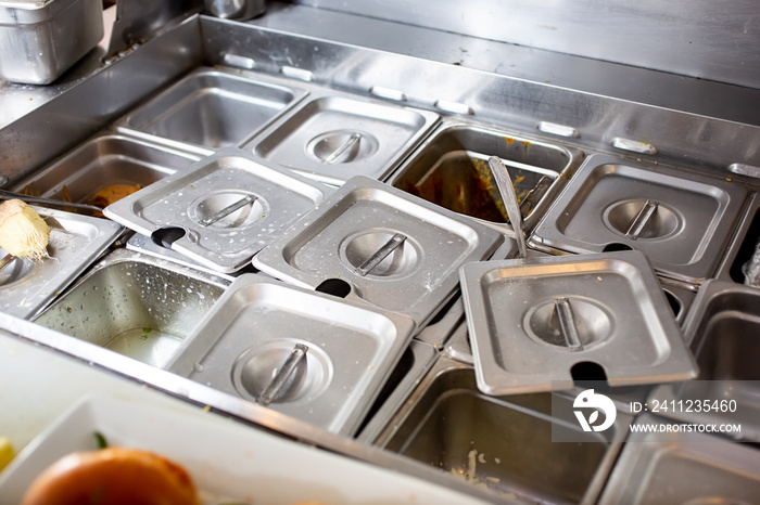 A view of food pan station in a messy fashion, in a restaurant kitchen setting.