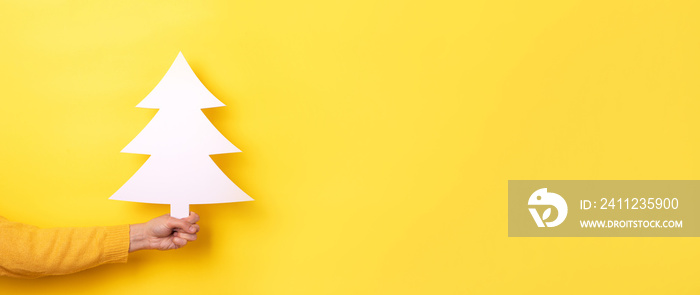 christmas tree in hand over yellow background, panoramic layout with space for text, happy new year 