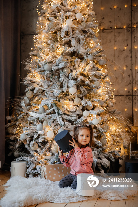 A little happy girl child kid is holding a present near a Christmas tree.