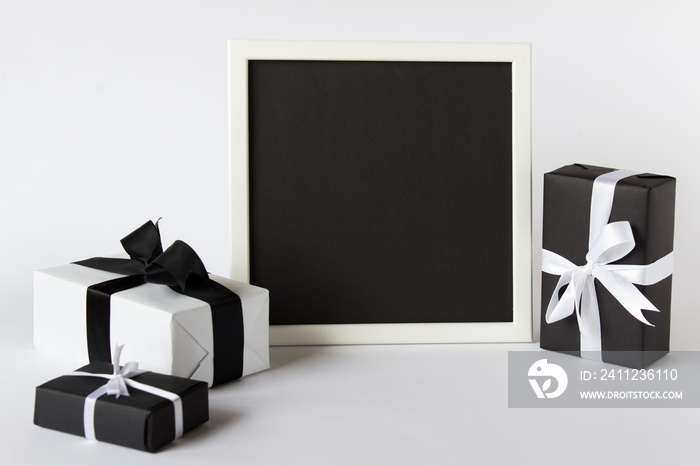 Presentation photo picture frame with black empty blank paper and three gift present boxes on white 