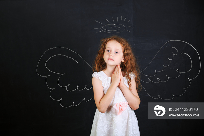 Cute girl near angel wings drawn on a blackboard.