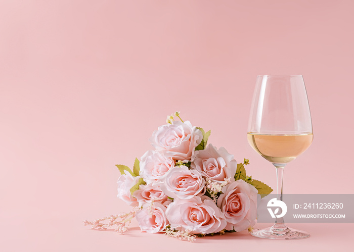 Bouquet of delicate rose flowers on pink background and glass of white wine.