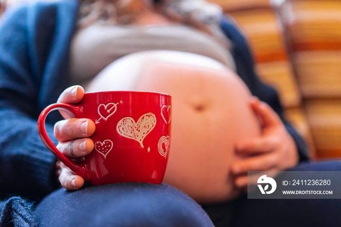 A low angle selective focus shot of a heavily pregnant woman enjoying a hot brew in novelty red vale