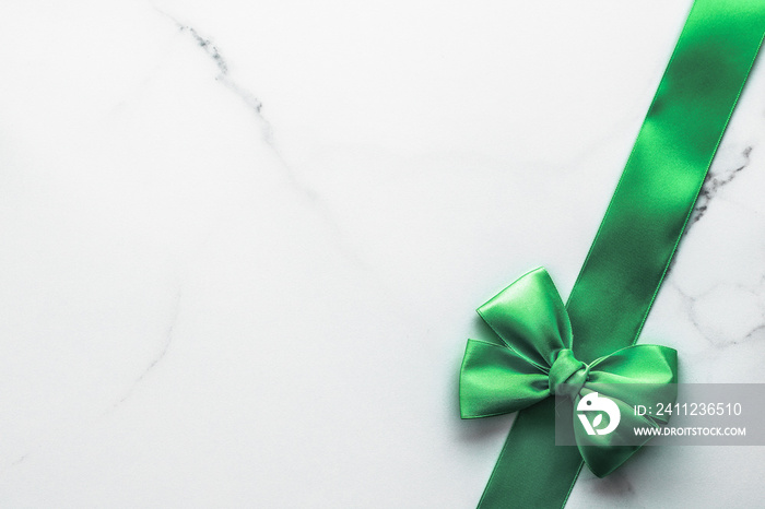 Green silk ribbon and bow on marble background, St Patricks day present or Christmas glamour gift de