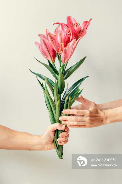 Mans hand giving bouquet of lilies flowers to womas hand