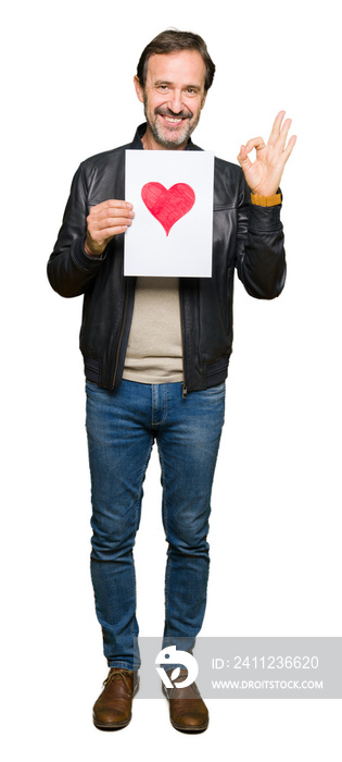 Handsome middle age man holding paper with red heart doing ok sign with fingers, excellent symbol