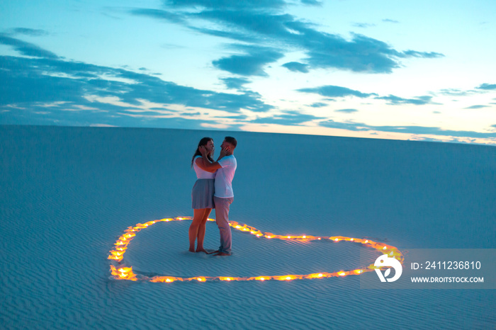 Couple in love romantic hugs in sand desert. Evening, romantic atmosphere, in sand burn candles in f