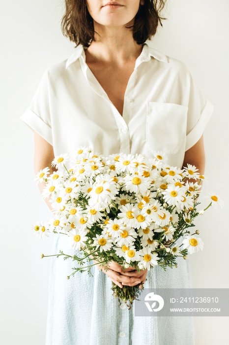 Young woman hold in hands bouquet of white chamomile daisy flowers on white background.