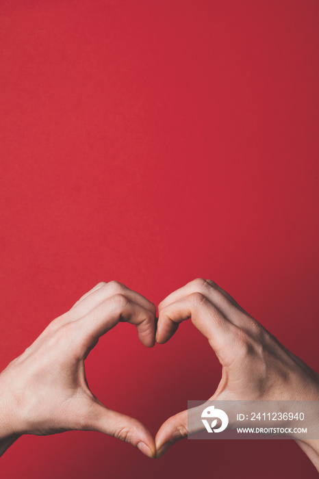 Female hands creating the shape of a heart over a red background.