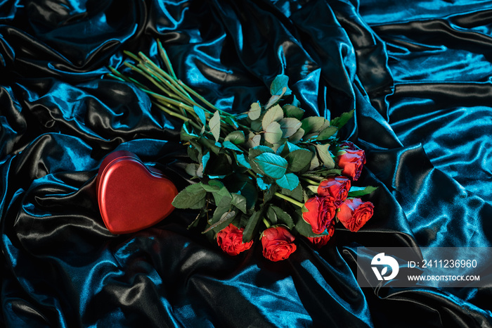 Top view of heart shaped box and roses on black bedding