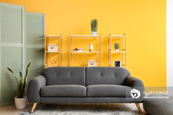 Interior of living room with folding screen, cozy sofa and shelving units near yellow wall