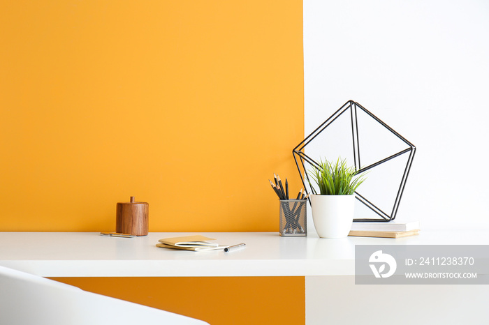 Stylish workplace with houseplant and stationery near color wall