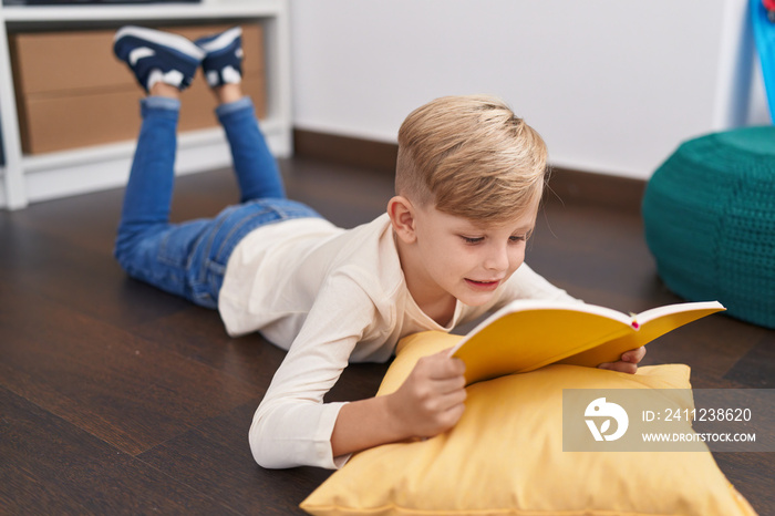 Adorable toddler reading book lying on floor at home