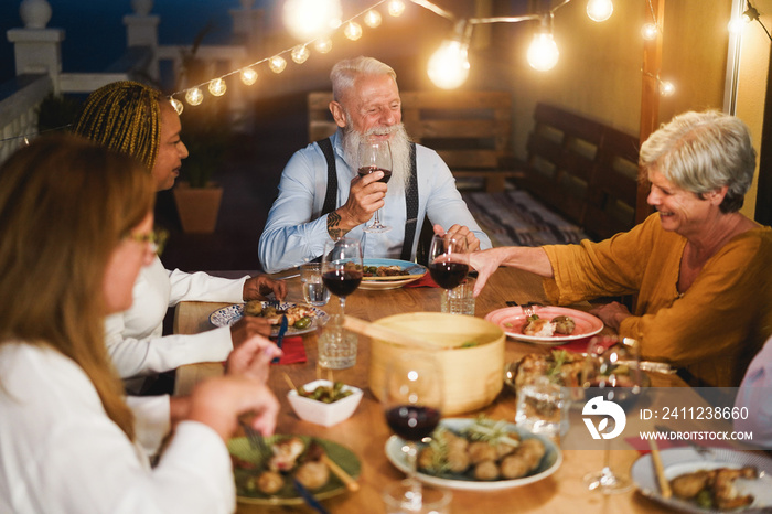 Happy senior people having fun at patio dinner - Multiracial friends eating on evening time - Focus 