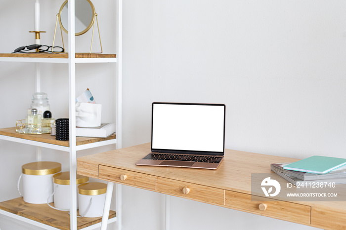 Laptop with blank white screen on the office table in home scandi interior. Stylish minimal workplac