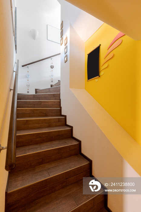 Brown stairs with yellow walls and wooden handrails