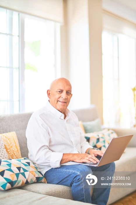 Senior handsome man smiling happy and confident. Sitting on the sofa using laptop at home