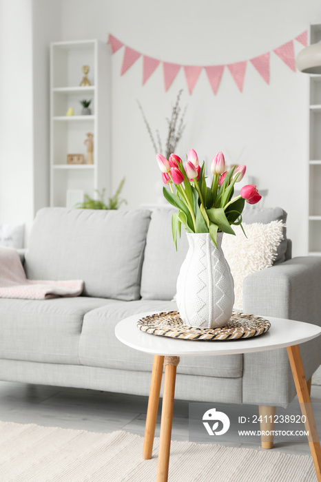 Vase with tulips on table in living room decorated for Easter celebration