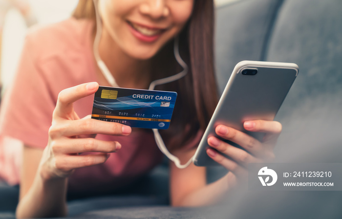 Happy young Asian woman holding credit card and using smartphone for shopping online with payment on