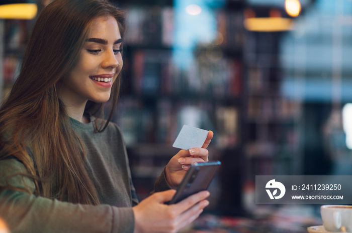 Woman using smartphone and a credit card for online shopping in a cafe