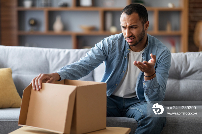 Wrong Parcel. Confused black man looking at open cardboard box at home