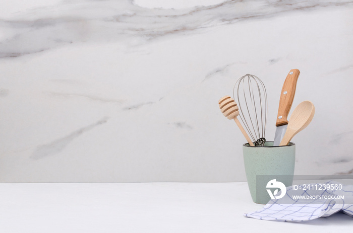 Closeup of bright blue cup and wooden spoon,honey dipper, whisk and khife in it, napkin on the white