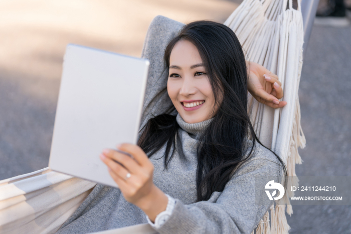 年轻女子躺在吊床上使用平板电脑