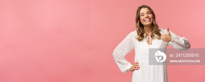 Enthusiastic lovely young woman in white cute dress, show thumb-up in approval, recommend product, smiling satisfied, leave positive review, impression, standing pink background