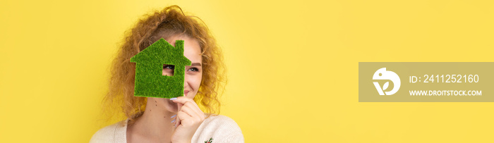 Happy house buyer. A young girl holds a model of a green house in her hands. The concept of green energy, ecology.