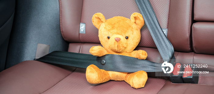 Yellow bear doll fastening seat belt during sitting inside a car and driving on the road. Car Seat, safety, trip, journey and transport concept