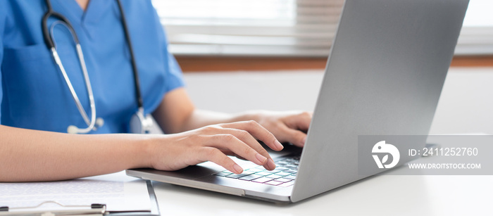 Veterinarian woman in blue uniform is using laptop to searching pet information and typing treatment