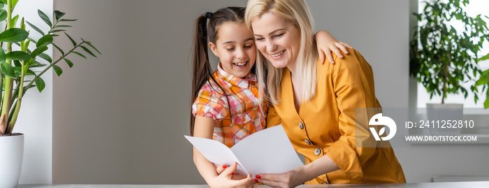 Happy women’s da. Child daughter is congratulating mom and giving her postcard. Mum and girl smiling and hugging. Family holiday and togetherness.