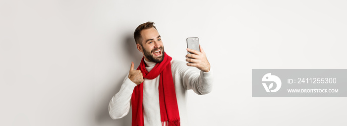 Happy bearded man video call and showing thumbs up at mobile phone, like christmas gift, talking online, standing over white background