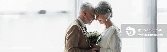 side view of bearded middle aged groom holding wedding bouquet with happy bride in white dress, banner