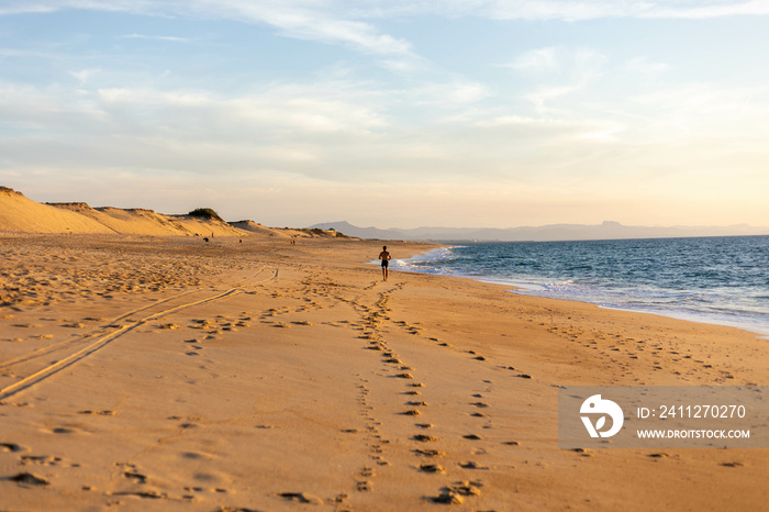 Une silhouette sur le plage marche face à l’océan avec des montagnes en fond, plage des Landes à Labenne