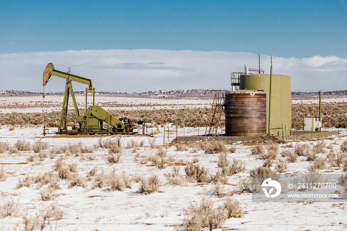 Lonely oil pump in the middle of a snow covered desert landscape on clear day in rural New Mexico