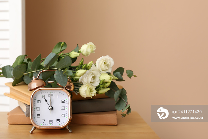 Bouquet of beautiful flowers, books and alarm clock on wooden table near color wall